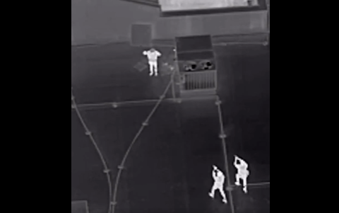 Thermal drone footage of individuals on an industrial rooftop at night